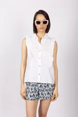 Blusa blanca sin mangas con cuello camisero y volados en los hombros.