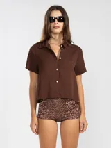 Camisa manga corta color marrón confeccionada en una mezcla de lino y tencel, con cuello camisero y cierre abotonado al frente.