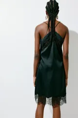 Vestido corto lencero de satén negro, con escote en V pronunciado y ribetes de encaje floral en el escote y el bajo. Cuenta con finos tirantes spaghetti cruzados en la espalda.
