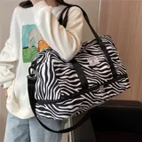 Bolso deportivo de viaje marca Zuomanni, con estampado animal print de leopardo en blanco y negro. Cuenta con doble asa de mano, correa de hombro ajustable y extraíble, y un compartimento inferior independiente con cierre.