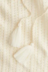 Chaleco de punto color blanco roto, sin mangas, con cuello polo y abertura en V con cordones terminados en borlas.