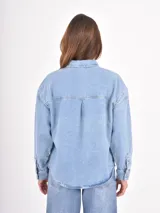 Camisa de jean de corte oversize, con cierre frontal de botones metálicos, cuello clásico y bolsillo frontal decorado con tachas plateadas.