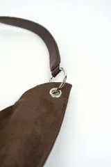 Bolso tipo hobo confeccionado en gamuza marrón, con diseño slouchy, asa corta de cuero y argollas metálicas plateadas.