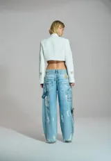Chaqueta corta de sastrería color blanco, con cuello mao, hombreras marcadas y cierre frontal mediante alamar metálico con diseño de flor y cadena.