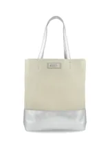 Cartera tipo tote de cuero color crudo con base y asas plateadas, de diseño vertical y rectangular con detalle de placa metálica con logo de la marca en el frente.