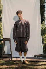 Buzo crewneck color chocolate, de tela rústica liviana, con estampado en el frente y la espalda. Presenta líneas blancas decorativas en el pecho y los brazos, y bordes deshilachados en los puños y el dobladillo.