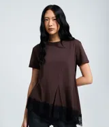 Remera marrón de algodón de manga corta y cuello redondo, con costuras delanteras visibles, diseño asimétrico y detalle de encaje negro en el ruedo.