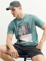 Remera verde petróleo de manga corta con estampa fotográfica de un edificio nevado. Corte clásico y cuello redondo.