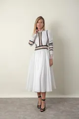Vestido midi blanco con detalles de encaje y vivos negros. Tiene cuello mao, mangas largas con puños de encaje y falda amplia con tul de armar.
