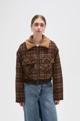 Campera corta de estilo bomber con estampado a cuadros en tonos marrones. Presenta cuello de corderito sintético, cierre frontal con cremallera, dos bolsillos frontales con solapa y puños y ruedo de tejido elástico acanalado.