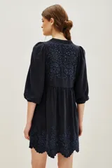 Vestido corto de viscosa color negro, con diseño holgado, mangas tres cuartos abullonadas y cuello en V. Presenta delicados bordados florales en tono azul oscuro en el pecho y en el ruedo, el cual termina con un borde festoneado.
