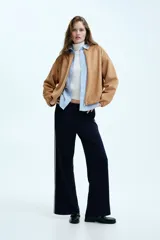 Chaqueta de punto pesado color tostado, con escote redondo, cierre frontal y bolsillos laterales. Presenta un diseño oversized con hombros caídos y terminaciones elásticas en puños y bajo.