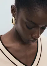 Jersey de punto fino en color crema con cuello de pico y detalles en contraste color marrón en el cuello y los puños. Presenta un diseño recto de manga larga.