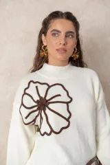 Buzo de tejido de punto color blanco, con cuello alto acanalado y mangas largas con puños ajustados. Presenta un diseño de flor grande en color chocolate aplicado en el frente.