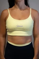 Top deportivo color amarillo claro con textura sutil y logo de la marca en color lila.