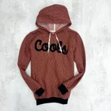 Canguro bordó con capucha, puños y cintura negros, cordones blancos y estampa negra con la palabra "Cools" en el pecho.