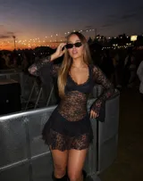 Vestido corto de encaje negro con transparencias, escote en V y mangas largas acampanadas. Presenta un diseño ajustado en el torso con una falda con volado en la parte inferior.