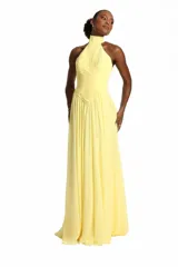 Vestido largo color amarillo, con cuello alto, diseño sin mangas y detalle de drapeado cruzado en el torso.