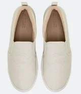 Championes slip-on color beige, sin cordones, con diseño capitoné en la parte frontal y suela blanca de goma.