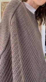 Poncho tejido en lana merino color marrón, con diseño de punto acanalado y terminación con flecos en el borde inferior. Incluye una pequeña etiqueta de cuero en la parte posterior.