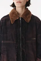 Campera de denim azul con corte oversized, cierre frontal y cuello de piel sintética marrón desmontable. Presenta detalles de volados en el frente, puños elásticos y logo bordado en el pecho.