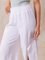 Pantalón blanco de lino con pretina ancha elastizada en punto smock, pierna ancha y ruedo con tajo.