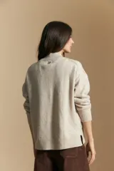 Sweater de punto color beige con diseño geométrico en relieve, cuello alto y mangas largas con puños acanalados.