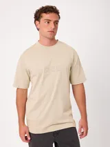 Remera holgada de algodón color beige con lavado ácido, cuello redondo ancho y diseño de tres pequeños círculos estampados en el pecho.