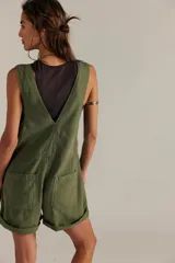 Enterito corto de denim en color verde militar, de silueta amplia y diseño tipo pinafore, con escote cuadrado, cierre frontal con cremallera, tirantes anchos y bolsillos funcionales.