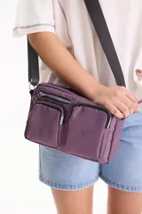 Bandolera color violeta con múltiples bolsillos frontales con cierre y correa ajustable negra.