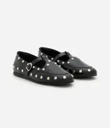 Zapato tipo salomé de color negro con acabado liso, puntera redondeada y suela plana. Presenta una tira central con hebilla metálica ajustable y está decorado con tachuelas metálicas plateadas distribuidas por toda la superficie.