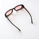 Lentes de sol con armazón rectangular de policarbonato marrón translúcido y cristales degradados en tonos rosados.