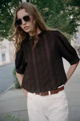 Blusa blanca de cuello alto con detalles de puntilla, manga corta abullonada y cierre posterior con botón.