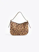 Cartera tipo hobo confeccionada en cuero con pelo vacuno estampado animal print. Presenta correa de hombro ajustable con detalles de hebillas metálicas en los laterales y cierre superior.