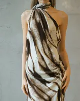 Vestido largo de satén con estampado abstracto en tonos tierra, escote halter con cuello alto y espalda descubierta. Presenta un diseño drapeado en la cintura y una abertura lateral profunda en la falda.