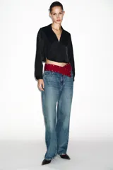 Camisa corta de tejido satinado color marrón, con cuello solapa, escote en pico y manga larga. Presenta cierre frontal con botones forrados a tono.