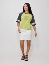 Remera bicolor Rusty de corte holgado y estilo deportivo, con cuerpo blanco y mangas raglán azules con doble raya blanca. Presenta estampado frontal con el texto 'RUSTY 85'.