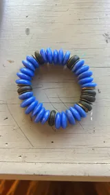 Set de tres pulseras elásticas con cuentas de madera en colores celeste, negro y rosa, con detalles de cuentas doradas y cuentas color crema.