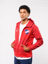 Campera deportiva Umbro del Club Nacional de Football, modelo Summit. Presenta un diseño con bloques de color en azul, rojo y blanco, con capucha, cierre frontal y bolsillos laterales con cierre. Incluye el logo de la marca y el escudo del club en el pecho.