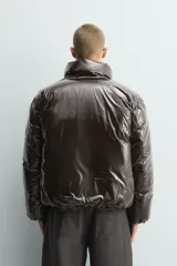Cazadora acolchada de corte boxy fit en tejido técnico con acabado brillante. Presenta cuello subido, cierre frontal de cremallera, bolsillos laterales de vivo y puños elásticos.