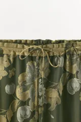 Pantalón de tiro medio confeccionado en mezcla de viscosa, con cintura elástica ajustable mediante cordón y diseño holgado. Presenta un estampado floral en tonos verde oscuro y beige, con detalle de panel contrastante en el bajo.