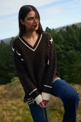 Sweater de punto trenzado color marrón con cuello en V, puños y ruedo acanalados en contraste color crudo. Presenta detalles de cordones cruzados en color crudo a lo largo de las mangas.