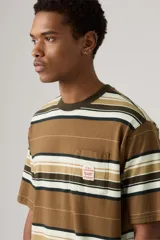 Remera de manga corta con cuello redondo y diseño de rayas horizontales en tonos marrón, blanco y negro. Presenta un bolsillo de parche en el pecho con una pequeña etiqueta decorativa blanca.