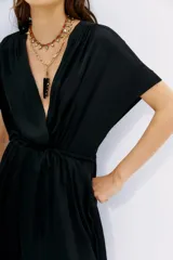 Vestido corto de color negro con escote cruzado, mangas cortas y cintura elastizada. Presenta un diseño de calce relajado y fluido.