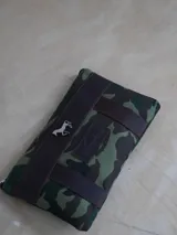 Sobre tipo cartuchera de lona con estampado de camuflaje y terminaciones en cuero marrón.