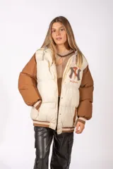 Campera puffer con diseño bicolor, cuerpo en color crudo y mangas en color marrón. Presenta cierre frontal con botones a presión, capucha integrada y puños de tejido acanalado a rayas. Incluye un parche bordado con las siglas NY en el pecho.