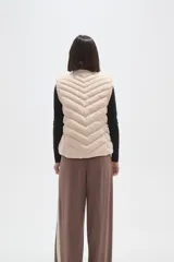 Chaleco acolchado de diseño capitoneado con cierre frontal y bolsillos laterales. Presenta un cuello alto y detalles de botones metálicos decorativos.