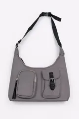 Cartera bandolera color gris de material sintético con correa ajustable negra y hebilla. Posee dos bolsillos frontales exteriores, uno con cierre y tirador largo y otro con solapa y hebilla decorativa.