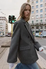 Blazer de corte oversize en color gris jaspeado, con cuello solapa, hombreras y cierre frontal cruzado con botones. Cuenta con bolsillos delanteros con solapa.