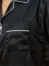 Pijama corto de satén negro, compuesto por una camisa de manga corta abotonada con solapas y ribetes blancos, y un short a juego con ribetes en el ruedo.